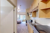 Located at 1536 Kerley Dr in San Jose, CA, this single-floor studio suite offers a thoughtfully designed, self-contained living space well-suited for extended stays. The open layout seamlessly connects each functional zone, creating an efficient and comfortable environment throughout.

The kitchenette is outfitted with light maple cabinetry, ample upper and lower storage, a two-burner electric cooktop, microwave, sink, compact refrigerator, and a built-in work desk with an ergonomic chair — making it as practical for remote work as it is for meal preparation. A wall-mounted flat-screen TV is positioned above the kitchen area for easy viewing.

The sleeping area features a large bed with a upholstered headboard, framed artwork, and a window with a roman shade that allows natural light while providing privacy. A ceiling fan adds comfort and airflow to the space.

A dedicated sitting area provides a cozy retreat, furnished with a plush armchair, a small round dining table with chairs, and warm ambient lighting from floor and wall-mounted lamps.

The bathroom is finished with stone-look tile flooring, a combination tub and shower with sliding glass doors, a wall-mounted sink, toilet, and a mirrored medicine cabinet with white cabinetry for storage. Warm yellow-toned walls carry consistently throughout the space, contributing to an inviting and cohesive ambiance.