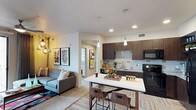 This single-floor residence offers a well-designed open-concept layout that seamlessly connects the living, dining, and kitchen areas. The kitchen is a standout feature, equipped with dark espresso cabinetry, granite countertops, a subway tile backsplash, black appliances, and an island with bar seating — ideal for both cooking and casual dining. Pendant lighting above the island adds a stylish focal point to the space. Open shelving provides additional storage and display opportunities.

The living area is warm and inviting, featuring a ceiling fan, sliding glass doors that open to a private balcony, and ample natural light. The balcony offers outdoor views, extending the living space beyond the interior.

The residence includes two bedrooms, each carpeted and fitted with ceiling fans and windows that bring in natural light. Both rooms offer a comfortable, restful atmosphere with generous layout.

Two bathrooms complement the bedrooms. One features a long vanity with dark cabinetry and a white countertop, paired with wood-look flooring. The second bathroom includes a tub-shower combination, dark cabinetry, and a full-length mirror that enhances the sense of space. Together, the rooms reflect a cohesive modern aesthetic with thoughtful design details throughout.