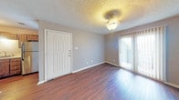 Located at 5249 US Highway 277 S in Abilene, Texas, this single-story unit offers a practical and well-organized layout designed for comfortable everyday living. The living area greets you at the front entry and is finished with rich, dark hardwood-style flooring that runs throughout the main living spaces. Large sliding glass doors dressed with vertical blinds allow natural light to fill the room, while a decorative ceiling light fixture adds a warm overhead glow. The textured ceiling is a consistent design element found throughout the home.

The kitchen is laid out in a galley style, featuring dark wood cabinetry, light-toned countertops, a stainless steel refrigerator, and black appliances including a range. A pass-through counter connects the kitchen to the living area, enhancing the open feel of the shared space. A window above the kitchen provides additional natural light.

The bedrooms are carpeted for comfort and warmth, each offering neutral gray walls and ceiling light fixtures. One bedroom features a walk-in closet, providing generous storage space. The bathroom is well-appointed with a tiled tub-and-shower combination, a dark wood vanity with a light countertop, and hardwood-style flooring that ties back to the main living areas. The overall color palette of soft grays and warm wood tones gives the unit a cohesive, move-in-ready appearance.
