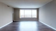 This one-bedroom, one-bathroom unit is thoughtfully laid out across a single floor, offering a comfortable and functional living environment. The spacious living room serves as the heart of the home, featuring dark hardwood-style flooring and a large picture window that frames sweeping elevated city views, flooding the space with natural light. A textured ceiling runs throughout the main living areas, adding a classic finishing detail.

The dining area connects seamlessly to the living room and features warm hardwood-style flooring, a pendant light fixture, and a pass-through window opening directly into the kitchen. The galley-style kitchen is well-equipped with white cabinetry, granite-style countertops, a mosaic tile backsplash, white appliances including a range, dishwasher, and refrigerator, and a drop ceiling with panel lighting above.

The bedroom is generously sized with plush carpeting, a large window offering additional city views, and access to both a walk-in closet and a full bathroom. The bathroom is finished with white tile flooring, a soaking tub with an overhead shower fixture, a pedestal-style vanity, and a large mirror, creating a clean and bright space.