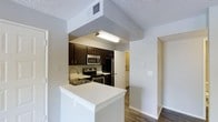 This single-story space showcases an open, well-organized kitchen that serves as the focal point of the layout. The kitchen is equipped with stainless steel appliances, including an electric range, over-the-range microwave, and refrigerator. Rich, dark espresso-toned cabinetry provides ample storage and creates a striking contrast against the light countertops. A white peninsula with an integrated sink extends into the space, offering additional workspace and a natural dividing point between the kitchen and adjacent areas. The textured ceiling adds a classic residential character, while the wood-look flooring throughout lends warmth and cohesion to the space. A hallway visible beyond the kitchen suggests access to additional rooms, contributing to the overall functional flow of the layout. The neutral white walls and light countertops keep the space feeling bright and open, while under-cabinet and overhead fluorescent lighting ensure the kitchen remains well-illuminated. The thoughtful layout balances practicality with an inviting atmosphere, making the kitchen a central and versatile area within the home.