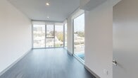 Located on West Pico Boulevard in Los Angeles, this contemporary single-floor residence showcases a clean, modern aesthetic with consistent design elements throughout. The living area is a standout feature, boasting expansive floor-to-ceiling windows that frame sweeping views of the surrounding Los Angeles cityscape, flooding the space with abundant natural light and creating an open, airy atmosphere. Durable wood-look flooring in a cool gray tone runs seamlessly throughout the unit, complementing the crisp white walls and clean lines.

The kitchen is well-appointed with a full suite of stainless steel appliances, including a gas range, over-the-range microwave, side-by-side refrigerator, and dishwasher. White cabinetry extends to the ceiling for generous storage, while dark countertops and a geometric tile backsplash add visual contrast and modern flair. A peninsula counter provides additional workspace and separation between the kitchen and living areas.

A corridor connects multiple rooms, each offering generous proportions and recessed lighting. The bathrooms are finished with clean white subway tile in the tub/shower surround, dark-countered vanities, and large mirrors, maintaining the unit's cohesive modern style.
