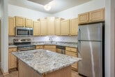 This single-floor, 2-bedroom, 1-bathroom residence offers a thoughtfully organized layout that balances practicality with comfortable living. The entry welcomes you directly into the kitchen and living area, where light wood-tone cabinetry, granite countertops, a stainless steel appliance suite, and a central island with an outlet create a functional and attractive culinary space. Recessed lighting and a chandelier add warmth to the open kitchen area, which flows into the living room. The living room is finished with rich hardwood-style flooring and features sliding glass doors that open to a lush, green outdoor view, filling the room with natural light. A second set of glass doors in an adjoining carpeted area further connects the interior to the outdoors. Both bedrooms are carpeted and generously proportioned, with the primary bedroom offering ample space and natural light through a large window overlooking mature trees. The second bedroom includes a built-in closet with dedicated shelving and hanging storage. The bathroom features light wood cabinetry, tile flooring, and a glass-enclosed shower. A dedicated laundry room with full-size washer and dryer completes this well-equipped residence.