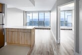 Located on an upper floor at 255 Glenlake Ave in Toronto's vibrant Junction neighbourhood, this single-storey unit offers sweeping panoramic views of the city skyline through expansive floor-to-ceiling sliding glass windows and doors. Natural light flows generously throughout the open-concept living spaces, which are finished with light grey laminate hardwood flooring and neutral-toned walls that create a clean, modern aesthetic.

The kitchen is thoughtfully designed with warm natural wood cabinetry extending to the upper walls, white quartz countertops, a central island with additional storage, and a full suite of stainless steel appliances including a refrigerator, dishwasher, and range. Large-format tile flooring grounds the kitchen area, distinguishing it from the adjoining living space.

The bedrooms feature the same light hardwood flooring, generous wall space, and access to the balcony via sliding glass doors, framing expansive city views. Built-in closets with double doors provide practical storage.

The bathroom is finished in a clean, all-white palette, featuring a soaker tub with shower, a wall-mounted vanity with an undermount sink, and a large mirror. The overall design throughout the unit is cohesive, contemporary, and bright.
