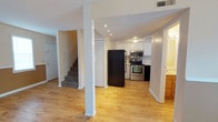 Located at 6000 Mabeline Road in Hanahan, South Carolina, this two-floor home offers a well-organized layout designed for comfortable everyday living. The main level features an open-concept design that connects the living area and kitchen seamlessly. Light-toned hardwood-style flooring runs throughout, lending warmth and continuity to the space. Structural columns define zones within the open floor plan without interrupting the sense of flow.

The living area is brightened by natural light streaming through sliding glass doors and windows, complemented by a ceiling fan overhead. Two-tone wall treatment — warm tan on the lower half and crisp white above — adds a distinct visual character to the room.

The kitchen is well-appointed with white cabinetry offering ample storage, light-colored countertops, and a suite of stainless steel appliances including a range, over-the-range microwave, and dishwasher, alongside a black refrigerator. Recessed lighting illuminates the workspace efficiently.

A carpeted staircase leads to the second floor, which continues the hardwood-style flooring and features multiple windows that allow generous natural light. The two-tone wall design is carried upward, maintaining a cohesive aesthetic throughout. The home also includes closet storage on the main level and a textured ceiling finish throughout.