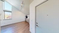 Located at 4122 36th Ave SW in Seattle's West Seattle neighborhood, this efficiently designed single-floor studio offers a surprisingly airy feel thanks to its dramatic vaulted ceilings that draw the eye upward and amplify the sense of space. The main living area features light-toned wood-style flooring throughout, crisp white walls, and a ceiling fan, creating a bright and clean atmosphere. A track lighting fixture near the entry provides focused, adjustable illumination across the open layout.

The kitchenette is thoughtfully appointed with light wood-grain cabinetry — including both base and upper storage units — a single-basin sink, an electric cooktop, a full-size stainless steel refrigerator, and a microwave, offering practical functionality within a compact footprint. Open shelving adds additional storage above the appliances.

The bathroom continues the modern aesthetic with wood-style flooring, a light wood vanity with a white countertop and undermount sink, a toilet, and a walk-in shower. A wall-mounted sconce provides warm lighting, while a window allows natural light to filter in. Grab bars and a towel bar add both convenience and accessibility. The unit also includes an electrical panel and a wall-mounted thermostat, ensuring all essential utilities are in place.