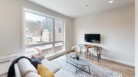 Located at 1314 Spring Garden St in Philadelphia's vibrant Spring Garden neighborhood, this thoughtfully designed one-bedroom unit makes efficient use of its compact footprint across a single floor. The open-concept layout seamlessly connects the living, dining, and sleeping areas, creating a cohesive and functional living environment.

The living area is anchored by a large picture window that floods the space with natural light and offers sweeping views of the Philadelphia cityscape. Wood-look flooring runs throughout the main living zone, complementing the neutral, warm-toned walls and recessed lighting overhead. A compact dining area with modern seating sits adjacent to the living space, maximizing the use of the floor plan.

The sleeping area is thoughtfully partitioned with built-in white cabinetry and open shelving above the bed, providing integrated storage without compromising the open feel of the unit. The bedroom connects directly to the bathroom, which features tile flooring and a shower with a curtain enclosure.

The kitchen is efficiently laid out along one wall, equipped with dark appliances and light cabinetry. Throughout the unit, the design prioritizes smart storage solutions and clean, modern aesthetics, making this a well-appointed urban residence in one of Philadelphia's dynamic neighborhoods.