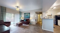 This single-story residence offers a thoughtfully designed layout that balances comfort and functionality across several distinct living areas. The living room serves as the heart of the home, featuring wood-look flooring, a ceiling fan, and a sliding glass door that floods the space with natural light while providing direct access to an outdoor patio area. The open flow connects seamlessly to the rest of the unit, creating an inviting and airy atmosphere.

The galley-style kitchen is efficiently organized with ample white cabinetry, granite-style countertops, a double basin sink, and a full suite of black appliances including a refrigerator, electric range, microwave, and dishwasher. Adjacent to the kitchen, the dining area features wood-look flooring, a pendant light fixture, large windows with decorative curtains, and tall accent mirrors that enhance the sense of space.

Both bedrooms are carpeted and generously sized, each equipped with ceiling fans, large windows with outdoor views, and ample natural light. The full bathroom includes white cabinetry, granite-style countertops, a wide vanity mirror, and a full tub-shower combination with wood-look tile flooring. A dedicated in-unit laundry room accommodates a full-size washer and dryer with overhead shelving for added storage.