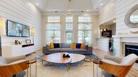 Located at 100 Madison Place Cir in Kernersville, NC, this thoughtfully designed single-floor space combines modern aesthetics with functional versatility across three distinct areas. The living room is the centerpiece of the space, boasting soaring tray ceilings, shiplap accent walls, and an abundance of natural light streaming through floor-to-ceiling windows adorned with sheer curtains. A sleek fireplace with a tiled surround serves as a focal point, complemented by light hardwood flooring that flows throughout. Large glass doors open to outdoor views, further enhancing the airy, open atmosphere. The kitchen features dark cabinetry with brushed nickel hardware, granite countertops, and stainless steel appliances, including a built-in microwave. A self-serve coffee station adds a welcoming, hospitality-forward touch. The office area provides a dedicated workspace, rounding out the functionality of this versatile layout. Warm pendant lighting and curated décor, including gold sculptural wall art and vibrant accent pieces, lend the space a polished, contemporary character. Overall, the space strikes a refined balance between comfort and sophistication.