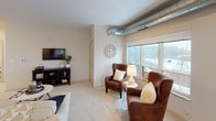 This thoughtfully designed single-floor residence blends modern industrial touches with warm, livable interiors. The open-concept layout connects the kitchen, dining, and living areas seamlessly, creating a welcoming and functional space. The kitchen is outfitted with dark cabinetry, granite countertops, a subway tile backsplash, a breakfast bar with pendant lighting, and a dedicated walk-in pantry — providing ample storage and style. Exposed silver ductwork runs through the main living areas, adding an industrial character that complements the contemporary design. Large windows throughout flood the space with natural light and offer outdoor views.

The living area features plush carpeting and a cozy seating arrangement, ideal for both relaxing and entertaining. The primary bedroom includes a ceiling fan and direct access to a bathroom, while the second bedroom offers a double closet and soft, neutral tones. A well-appointed bathroom with a dark vanity and tile flooring serves the secondary spaces. Wood-look flooring runs through the entryway and hallways, creating a smooth transition between rooms. A dedicated in-unit laundry area with a full-size washer and dryer rounds out the practical amenities of this comfortable and stylish residence.
