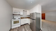 This single-floor, 2-bedroom, 1-bathroom unit at 171 Glenora Dr in Rochester, NY offers a practical and efficiently arranged layout. The combined kitchen and living room area anchors the space, with the kitchen featuring white cabinetry, dark granite-style countertops, wood-look vinyl flooring, a white electric range with built-in microwave, and a stainless steel refrigerator. The living room is carpeted in neutral tones and receives natural light through a window overlooking mature trees, with a wall-mounted air conditioning unit providing supplemental climate control.

A hallway connects the main living area to the two bedrooms and bathroom. The primary bedroom offers a comfortable footprint with carpet flooring, a sliding-door closet, and a baseboard heating unit. The second bedroom is more compact, also carpeted, with a window admitting natural light and its own baseboard heater. Both bedrooms maintain a neutral color palette. The bathroom features a tub-shower combination with tiled surround walls in a classic cream tone. Baseboard heating is present throughout the unit, ensuring consistent warmth during Rochester's colder months.