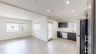 This well-designed 2-bedroom, 2-bathroom single-floor unit offers a clean, modern aesthetic throughout its thoughtfully arranged layout. The open-concept living and kitchen area is anchored by light wood-look flooring and recessed lighting, creating a bright and welcoming atmosphere. The kitchen is a standout feature, boasting rich dark cabinetry with sleek hardware, light countertops, and a full suite of stainless steel appliances including a refrigerator, range, microwave, and dishwasher. A window above the sink allows natural light to fill the space. The living area flows seamlessly from the kitchen and provides access to a private balcony through a glass-paneled door, offering views of the surrounding courtyard. Both bedrooms are generously proportioned, featuring plush carpet flooring, large windows with horizontal blinds, and sliding closet doors for convenient storage. The primary bedroom is particularly spacious, with dual windows framing pleasant neighborhood and mountain views. The two bathrooms are finished in a clean, minimalist style, each featuring a tiled tub-shower combination with chrome fixtures and light wood-look flooring. Throughout the unit, crisp white walls and natural light contribute to an airy, move-in-ready ambiance.