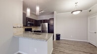 This single-floor residence offers a thoughtfully designed open-concept layout that seamlessly connects the kitchen and living areas. The kitchen is a standout feature, showcasing rich dark cabinetry, a mosaic tile backsplash, granite countertops, and a full suite of stainless steel appliances, including a refrigerator, range, and microwave. A peninsula with an integrated sink and pendant lighting above adds both functionality and style, making it an ideal space for cooking and entertaining.

The living area is bright and welcoming, finished with plush carpeting, crown molding, and a ceiling fan. A set of French doors allows natural light to pour in and provides a direct connection to the outdoors. Adjacent to the living space, a flexible room features wood-look flooring, crown molding, and a built-in bookshelf, offering versatile use as a home office or den. A louvered closet door adds to its practicality.

The bedrooms continue the warm, neutral palette with soft carpeting and natural light from window treatments. The bathroom is well-finished with matching dark cabinetry, granite countertops, a wide vanity mirror, and a full soaking tub with a shower. Wood-look flooring ties the bathroom together with the rest of the home's cohesive design aesthetic.