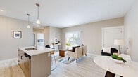Located at 3800 E Campus Ave in Holland, MI, this well-designed 3-bedroom, 2-bathroom unit offers a thoughtfully planned single-floor layout. The open-concept living and kitchen area serves as the heart of the home, finished with light wood-look flooring that extends throughout the main spaces. The kitchen is equipped with stainless steel appliances, including a refrigerator, range, and built-in microwave, complemented by sleek gray cabinetry, white quartz countertops, and a peninsula island with bar seating and pendant lighting overhead. The living room is bright and inviting, anchored by a large sliding glass door that floods the space with natural light and provides direct access to an outdoor area with open green views. The primary bedroom features wide windows with outdoor views and plush carpeting, creating a comfortable retreat. The additional bedrooms are equally well-lit, with large windows and carpet flooring, offering flexibility for sleeping, office, or flex use. The bathrooms are cleanly finished, with one featuring a full shower-tub combination. Warm neutral wall tones throughout lend a cohesive, modern aesthetic to the entire unit.