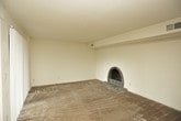 This single-floor residence offers a well-organized layout with a variety of functional spaces throughout. The living area is a standout, featuring plush wall-to-wall carpeting, a ceiling fan, and a striking arched brick fireplace with a raised hearth as a focal point. Built-in shelving lines one wall, providing practical storage and display space. Sliding glass doors with vertical blinds allow natural light to fill the room and offer access to the outdoors.

The kitchen is equipped with warm-toned wood cabinetry offering generous upper and lower storage, stone-patterned laminate countertops, and a double-basin stainless steel sink. Black appliances, including a gas range, built-in microwave, and dishwasher, complement the cabinetry. Tile flooring completes the practical workspace.

The bedroom is spacious and carpeted, featuring a large mirrored sliding closet that enhances the sense of space. A window allows natural light to brighten the room. The bathroom includes a wood-toned vanity with stone-patterned countertop, a large mirror, tile flooring, and a full tub and shower combination with brushed nickel fixtures. The overall ambiance is neutral and move-in ready.