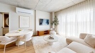 Located at 1555 Boul Chomedey in Laval, QC, this well-appointed 2-bedroom, 2-bathroom unit offers a thoughtfully designed single-floor layout with a clean, contemporary aesthetic. The open-concept living and kitchen area serves as the heart of the space, where light hardwood flooring flows seamlessly underfoot and exposed concrete ceilings add an industrial yet refined character. Floor-to-ceiling sheer curtains frame expansive windows in the living area, flooding the space with natural light and creating a bright, airy atmosphere. The modern kitchen is equipped with flat-front cabinetry in warm taupe tones, a white quartz waterfall island with bar seating, a matte black faucet, and stainless steel appliances, all finished with sleek pendant lighting overhead. The primary bedroom is generously proportioned, featuring large windows with sheer drapery and exposed concrete beam accents. The second bedroom also benefits from ample natural light and its own closet. Both bathrooms are finished to a high standard: one features a glass-enclosed walk-in shower with large-format tiles and matte black hardware, while the other offers a full soaking tub and shower combo with a wood-accented vanity. A welcoming hallway connects the rooms, completing this stylish and functional layout.