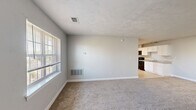 Located at 1568 North King Street in Hampton, Virginia, this single-floor, two-bedroom, one-bathroom home offers a practical and comfortable layout with consistent neutral finishes throughout. The living area is carpeted in warm beige tones and benefits from natural light through a multi-pane window fitted with blinds, creating a bright and welcoming atmosphere. The kitchen features crisp white shaker-style cabinetry, light granite-look countertops, a stainless steel sink, and black appliances including a range, over-the-range microwave, and refrigerator. Light tile flooring grounds the kitchen space, which opens directly to the living area for a connected feel. Both bedrooms are carpeted and painted in soft grey tones, each with a window allowing natural light. The primary bedroom offers generous floor space, while the second bedroom is equally well-proportioned with a closet. The bathroom is clean and functional, featuring a full tub/shower combo with bright white surround. A dedicated laundry area houses a stacked washer and dryer unit alongside built-in wire shelving, adding convenient in-unit storage. The home's cohesive light grey walls and white trim give it a clean, move-in-ready appeal throughout.