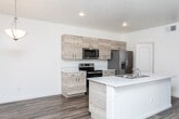 This single-floor unit at 9555 W State St in Garden City, Idaho, presents a contemporary design with a clean, neutral palette throughout. The open-concept kitchen and living area serves as the heart of the space, where light wood-tone cabinetry extends to the ceiling, offering generous storage alongside stainless steel appliances, including a range, over-the-range microwave, and french door refrigerator. A central island with a white countertop and integrated sink provides additional workspace and casual seating potential. Warm wood-look vinyl flooring extends through the kitchen and living area, which benefits from a sliding glass door that invites natural light and outdoor views.

A dedicated hallway connects the bedrooms, each finished with plush neutral carpeting and windows fitted with blinds that frame views of surrounding greenery. The layout accommodates multiple bedrooms, supporting flexible use of the space.

Two bathrooms feature the same light wood-tone cabinetry with white countertops, wood-look flooring, and clean white fixtures. One bathroom includes a soaking tub, while the other offers a more streamlined configuration. Together, the rooms maintain a consistent, modern aesthetic throughout the unit.
