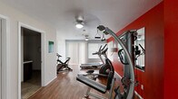 This fitness center at 4598 W Fairway Dr in Coeur d'Alene, Idaho, offers a well-equipped workout space designed to support a range of exercise routines. The single-floor layout makes efficient use of its footprint, providing a focused and functional environment for residents or members.

The interior is defined by bold red accent walls that energize the space, complemented by neutral gray and white tones on the surrounding walls and trim. Rich, dark hardwood-style flooring runs throughout, adding warmth and durability underfoot. A textured white ceiling with ceiling fans ensures comfortable airflow during workouts.

The main workout area is outfitted with a variety of cardio and strength training equipment, including a treadmill, elliptical trainer, stationary cycle, and a multi-function cable resistance machine. A large wall-mounted mirror enhances the sense of space and allows users to monitor their form. Natural light filters in through windows dressed with vertical and horizontal blinds, keeping the atmosphere bright without glare.

A dedicated women's restroom is accessible directly from the workout floor, adding convenience to the facility. The overall design is practical and motivating, with a clean, energetic aesthetic that supports an active lifestyle.