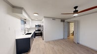 Located at 205 E 4th St in the heart of downtown Austin, Texas, this one-bedroom, one-bathroom unit offers a thoughtfully designed layout that maximizes every square foot. Light wood-style flooring runs throughout, creating a cohesive and contemporary feel across all rooms.

The open living area is bright and welcoming, featuring a ceiling fan with a wood-toned blade, crown molding details, and a front entry door with transom glass panels that allow natural light to filter in. A window with horizontal blinds further enhances the airy atmosphere.

The kitchen is a standout feature, finished with a two-tone design of navy lower cabinetry and white upper cabinets paired with crisp white countertops. Stainless steel appliances — including a gas range, built-in microwave, and refrigerator — provide a fully equipped cooking space. A deep undermount sink with a modern gooseneck faucet and a window above the counter complete the kitchen's functional and stylish design.

The bedroom is a quiet, well-proportioned retreat with a large window dressed in white horizontal blinds, allowing for ample natural light and privacy control.

The bathroom echoes the design language of the kitchen, featuring a navy vanity with a white countertop, an undermount sink, a framed mirror, and industrial-style three-bulb vanity lighting. The clean white walls and wood-style flooring tie the room together cohesively.
