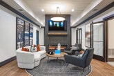 Located at 1570 Sheridan Rd NE in Atlanta, GA, this thoughtfully designed single-floor space blends contemporary aesthetics with inviting warmth. The interior is unified by rich wood-look flooring that flows seamlessly throughout, complemented by crisp white walls, bold dark trim, and carefully curated large-scale artwork that adds visual depth and character to every area.

The entryway makes an immediate impression with a dramatic dark brick accent wall showcasing an oversized abstract painting in warm amber and rust tones. A gallery-style corridor leads further into the space, lined with striking black-and-white artwork that creates a sophisticated sense of arrival.

The main lounge area serves as the heart of the space, anchored by a floor-to-ceiling dark brick fireplace with a linear electric hearth and a mounted flat-screen television above a natural wood mantel. A shiplap ceiling with a central pendant light adds texture and warmth overhead, while large windows allow natural light to filter in. The seating arrangement — featuring a curved cream sofa, deep charcoal accent chairs, and a round wood coffee table — creates an intimate yet open atmosphere.

A glass-enclosed office area provides a dedicated workspace without sacrificing visual connectivity to the rest of the space. The entry vestibule, framed by tall dark-paneled doors with sidelights, offers a welcoming and polished transition from the exterior into this well-appointed interior.