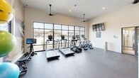 Located at 451 Hill Branch Rd in Flat Rock, NC, this fitness center offers a thoughtfully designed workout environment spread across a single floor. The space is anchored by a row of cardio machines — including treadmills, ellipticals, and stationary bikes from TRUE Fitness — positioned along a striking wall of floor-to-ceiling glass windows that frame views of the outdoor amenity area, flooding the room with natural light. Pendant-mounted ceiling fans and recessed lighting complement the bright, airy atmosphere throughout.

The strength training area is equally well-appointed, featuring a cable machine, a full dumbbell rack, kettlebells, medicine balls, resistance bands, and a multi-functional storage rack with TRX suspension trainers and a weighted sandbag. A large, artistic abstract mural spans one wall, adding a bold visual element to the space and contributing to an energetic yet polished ambiance. Wall-mounted flat-screen TVs are positioned throughout for entertainment during workouts.

The flooring consists of durable dark rubberized material suited for high-traffic exercise use. Glass double doors connect the fitness center to an adjacent facility, enhancing its accessibility. The overall design balances functionality with contemporary aesthetics, making it a versatile space for a full range of fitness activities.