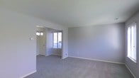 Located at 800 Trenton Road in Langhorne, Pennsylvania, this two-floor property offers a clean, neutral aesthetic throughout its interior spaces. The main living area is finished with plush wall-to-wall carpeting in a soft gray tone, providing a warm and comfortable foundation for the room. The walls are painted in a light, muted gray that lends a calm and cohesive atmosphere across the space. An open passageway connects the living area to an adjacent dining or entry space, which features a classic chandelier and a window that allows natural light to filter in, brightening the interior. Clean white trim and baseboards provide a crisp contrast against the soft wall tones, contributing to a tidy and well-maintained appearance. The layout across two floors offers a practical separation of living and private spaces, making the home well-suited for a range of occupants. The overall ambiance is understated and move-in ready, with a neutral palette that serves as a versatile backdrop for a variety of interior styles and furnishings.