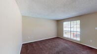 This single-floor residence features two bedrooms and two full bathrooms within a well-organized layout. The living and dining area is carpeted in a deep brown tone, complemented by neutral beige walls and a textured popcorn ceiling. A large window allows natural light to flow into the main living space, providing views of the surrounding exterior. A pendant light fixture above the dining area adds a subtle design touch, while an open passageway connects the living space directly to the kitchen.

The kitchen is equipped with white cabinetry, light-toned countertops, a white electric coil range, and a refrigerator. A pass-through window connects the kitchen to the living and dining area, enhancing the open feel of the space.

Both bedrooms are comfortably sized with the same dark carpet and neutral wall tones found throughout the unit. Each room benefits from window access, providing natural light and outdoor views. The bedrooms are well-suited for furnishing with standard bedroom sets.

The two bathrooms each offer functional layouts. One features a tub-shower combination with chrome fixtures and a light countertop vanity with white cabinetry. The second bathroom mirrors a similar design with tile flooring and a shower-curtain enclosure. Overall, the unit maintains a clean, neutral aesthetic throughout.
