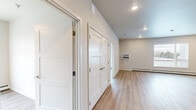 This 2-bedroom, 1-bathroom unit offers a clean, modern design with light hardwood-style flooring running consistently throughout every room. The open-concept kitchen and living area serves as the heart of the unit, featuring a well-equipped kitchen with gray shaker-style cabinetry, light stone countertops, a subway tile backsplash, and a full suite of stainless steel appliances including a refrigerator, range with a wall-mounted range hood, dishwasher, and built-in microwave. The adjoining living area is bright and spacious, with a wall-mounted air conditioning unit and a large window that brings in natural light and outdoor views.

Both bedrooms are comfortably sized, each equipped with baseboard heating and windows with blinds. The primary bedroom features a high horizontal window, while the second bedroom includes a wall-mounted A/C unit alongside a large window. Each bedroom has access to a dedicated closet fitted with wire shelving systems for practical storage.

The hallway connecting the rooms is lined with clean white panel doors and includes additional closet space. The bathroom continues the unit's modern aesthetic with hardwood-style flooring, a dark vanity, and accessibility-friendly grab bars. The overall design is neutral, bright, and move-in ready.