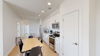 This contemporary single-floor residence offers a thoughtfully designed layout spanning a generous footprint across multiple well-defined rooms. The interior is characterized by a clean, modern aesthetic with crisp white walls, light hardwood flooring, and recessed lighting throughout, creating a bright and cohesive atmosphere.

The kitchen is a standout feature, fitted with full-height white shaker cabinetry, a herringbone-patterned tile backsplash, light countertops, and a complete suite of stainless steel appliances including a refrigerator, electric range, and over-the-range microwave. An adjacent dining area accommodates a rectangular wood-top table with seating for several guests.

The living room is a comfortable, light-filled space featuring large windows with horizontal blinds that frame views of the surrounding urban neighborhood, allowing abundant natural light to fill the room. The bedrooms are similarly well-lit, each benefiting from dual windows overlooking the cityscape and light hardwood floors.

The bathrooms maintain the home's consistent modern design language, with white vanities featuring black hardware, undermount sinks, large mirrors, and wood-look flooring. At least one bathroom includes a full bathtub with classic white subway tile surround. A central hallway connects all rooms, providing a logical and efficient flow throughout the residence.