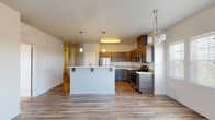 Located at 4909 N Elsinore Ave in Meridian, Idaho, this contemporary single-floor unit offers a well-designed, open-concept layout with modern finishes throughout. The kitchen serves as the centerpiece of the living area, showcasing two-tone cabinetry in warm wood and dark gray tones, stainless steel appliances including a gas range, microwave, and refrigerator, and light quartz countertops. A kitchen island with bar seating provides additional functionality, while stylish pendant lighting adds a polished finishing touch. Wood-look plank flooring extends throughout the main living and kitchen areas, creating a cohesive and easy-to-maintain surface. A dining area adjacent to the kitchen benefits from a large bank of windows fitted with blinds, filling the space with natural light. The bedrooms are finished with plush carpet and feature windows that bring in additional daylight. The primary bathroom is a standout, offering a dual-sink vanity with quartz countertops, dark wood cabinetry, a subway tile backsplash, and a wide mirror with overhead lighting. A secondary bathroom includes wood-look flooring, a tub-shower combination, and a window for natural ventilation. The overall ambiance is clean, modern, and move-in ready.