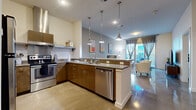 This contemporary single-floor residence is thoughtfully designed with an open-concept layout that seamlessly connects the kitchen and living area. The kitchen is well-appointed with warm wood cabinetry, granite countertops, stainless steel appliances including an electric range with overhead hood and a dishwasher, and a peninsula island with pendant lighting above. Polished concrete floors flow throughout the entire space, lending a sleek, modern aesthetic.

The living room is bright and welcoming, benefiting from floor-to-ceiling sliding glass doors that open to a private balcony, filling the space with natural light and offering outdoor views. The bedroom features a ceiling fan, a grey accent wall, and polished concrete floors, creating a calm and stylish retreat.

The bathroom includes a full soaking tub with tiled surround, granite vanity countertop, and direct access to a spacious walk-in closet with built-in shelving and hanging rods. A dedicated laundry area houses a stacked washer and dryer unit tucked neatly behind bi-fold doors. Additional storage is provided by a built-in open shelving nook. The overall ambiance of the residence is clean, modern, and functional.