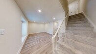This two-story home features a thoughtful layout spread across two well-proportioned floors. The main level hosts an open-concept kitchen and living area finished with light hardwood-style flooring and recessed lighting. The kitchen is a standout, equipped with white shaker cabinetry, stainless steel appliances, a subway tile backsplash, and a central island topped with granite countertops. A dedicated laundry room on this level includes a full-size washer and dryer alongside built-in shelving. The main floor also includes a bedroom with hardwood-style flooring and a full bathroom.

The upper level contains the remaining two bedrooms, including the primary bedroom, along with two additional bathrooms. Bedrooms on this floor feature plush carpeting and double-door closets with built-in rods. The bathrooms are finished with white vanity cabinetry, granite countertops, and tub-shower combinations with tiled surrounds. A carpeted staircase with a white balustrade connects the two floors. Throughout, the home maintains a clean, neutral palette of warm whites and beige tones, contributing to a bright and cohesive overall ambiance.