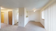 This single-floor residential unit offers a functional and well-organized layout designed for comfortable everyday living. The living room serves as the heart of the space, featuring wall-to-wall carpeting, a ceiling fan, a baseboard heating unit, and a classic brick fireplace flanked by a sliding glass door that opens to an outdoor balcony, allowing natural light to fill the room. A half-wall pass-through connects the living area to the kitchen, which includes white cabinetry, a refrigerator, and a range, with tile flooring that transitions cleanly from the carpeted areas. The bedroom is a quiet, well-proportioned room with plush carpeting, a window fitted with blinds that brings in natural light, a baseboard heater, and a sliding wood-panel closet with a built-in shelf and hanging rod. The bathroom features durable tile flooring in earthy tones, a toilet, a bathtub with a shower surround, and recessed lighting overhead. A hallway connects the main areas of the unit, with a wood-panel door providing separation between spaces. Throughout the unit, textured ceilings and neutral white walls provide a clean, move-in-ready backdrop that is easy to personalize.