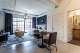 Located in the heart of Atlanta, GA, this single-floor urban residence seamlessly blends industrial character with refined contemporary design. The open-concept layout connects the living, dining, and kitchen areas into a cohesive and functional living space, with exposed ceiling infrastructure and polished concrete floors lending an authentic loft aesthetic.

The living area makes a bold statement with deep navy accent walls, a plush channel-back sofa, and a wall-mounted television, all anchored by a vintage-inspired patterned area rug. The kitchen is thoughtfully appointed with warm wood-toned cabinetry, a white subway tile backsplash, stainless steel appliances, open floating shelves, and light countertops — a practical yet attractive space for cooking and entertaining.

The bedroom exudes a boutique hotel ambiance, featuring large industrial-framed windows that flood the room with natural light and offer urban views of the Atlanta skyline. A geometric pendant chandelier, a tufted upholstered bed, and an elegant wall sconce complete the sophisticated atmosphere.

The bathroom is finished with floor-to-ceiling subway tile, a sleek glass-enclosed walk-in shower, and neutral tile flooring, offering a clean and modern retreat. Together, these elements create a space that is both visually striking and highly livable in one of Atlanta's vibrant urban neighborhoods.