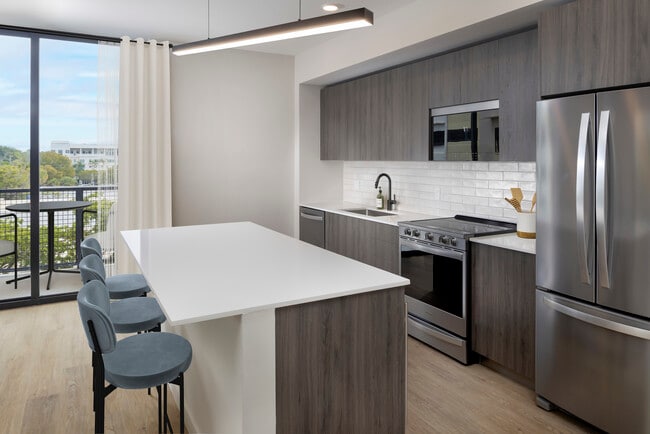 Colección Upgrade II Cocina de apartamento de tres habitaciones con gabinetes color espresso, placa para salpicaduras de azulejos blancos, encimera de cuarzo blanco y piso de tablones de vinilo de superficie dura - Avalon South Miami