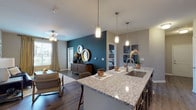 This single-floor residence offers a thoughtfully designed open-concept layout that seamlessly connects the kitchen, dining, and living areas. The kitchen serves as a central hub, featuring a large granite-topped island with pendant lighting overhead, dark espresso cabinetry, a subway tile backsplash, stainless steel appliances, and wood-look flooring. The island provides bar seating for casual dining, while the adjacent living area is anchored by a bold teal accent wall and natural light from large windows. The living room offers comfortable proportions with wood-look flooring and a ceiling fan.

The primary bedroom includes plush carpet, a dark accent wall, and a walk-in closet with built-in shelving. A secondary bedroom features carpet, a large window with natural views, and ample storage space. Both bathrooms are finished with granite countertops, dark cabinetry, and well-lit vanity mirrors. A dedicated laundry room with a full-size washer is conveniently accessible from the kitchen corridor. Throughout the space, consistent use of granite surfaces, dark cabinetry, and neutral wall tones creates a cohesive and modern aesthetic.