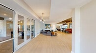 Located at 11201 Capital Blvd in Raleigh, NC, this thoughtfully designed amenity space offers a substantial single-floor footprint comprising four distinct living areas and a connecting hallway. Light-toned hardwood-style flooring flows consistently throughout, unifying the various zones into a cohesive environment.

The main lounge areas are anchored by stylish contemporary furnishings, including tufted velvet sofas, gold-accented coffee tables, and curated wall art that adds vibrant color and character. One area features floor-to-ceiling glass windows and doors that frame outdoor views of a landscaped courtyard and pool area, flooding the space with natural light. A dedicated social lounge with bar-height seating and bistro tables provides an inviting setting for casual gatherings.

A game room with a dark accent ceiling and recessed lighting houses a prominent air hockey table, offering a recreational retreat within the overall space. A cozy banquette nook with marble-topped tables provides an intimate dining or meeting area. A hallway connects the zones and includes a dual water fountain station accented by vibrant artwork.

Additional areas feature an open-plan layout with a kitchen bar, stone-clad accent wall, built-in media wall with fireplace, and ceiling fans — combining comfort with modern design. The overall ambiance is bright, welcoming, and contemporary throughout.