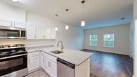 This single-floor unit in Mechanicsville, Virginia, offers a thoughtfully designed layout encompassing two bedrooms, one bathroom, a kitchen, living room, hallway, and closet. The open-concept kitchen and living area serves as the heart of the home, featuring a central island with granite-style countertops, an undermount sink, and pendant lighting overhead. White shaker-style cabinetry lines the kitchen walls, complemented by a full suite of stainless steel appliances including a refrigerator, range, microwave, and dishwasher. Light wood-tone flooring runs throughout the main living areas, creating a bright, cohesive aesthetic.

The living room adjoins the kitchen seamlessly, receiving natural light through multiple windows. Both bedrooms are carpeted and feature neutral walls; the primary bedroom offers a comfortable footprint with windows overlooking the outdoors. A louvered closet door provides storage access in one of the bedrooms. The shared bathroom includes a full tub/shower combination, a vanity with white cabinetry, and light wood-tone flooring. The overall design is clean, modern, and neutral throughout.