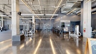Located at 1220 Second Ave N in Nashville's Germantown neighborhood, this single-floor fitness facility offers a generously sized, open-concept layout designed to accommodate a wide range of training activities. The space features an industrial-inspired aesthetic, with exposed concrete ceilings, structural columns, large ductwork, and polished concrete floors throughout much of the facility, complemented by rubber flooring in dedicated training zones.

Floor-to-ceiling glass garage doors and expansive windows line the exterior walls, flooding the space with abundant natural light and offering direct views of the surrounding Nashville streetscape. The open floor plan is divided into distinct functional zones: a dedicated strength and free weights area stocked with kettlebells, barbells, dumbbells, and weight racks; a spacious open training floor suited for group or functional fitness; a cardio section equipped with treadmills, stair climbers, stationary bikes, and ellipticals; and a cable and selectorized machine area supported by structural columns.

Motivational phrases are displayed prominently on the walls, reinforcing the facility's training culture. Additional amenities include water fountains, restrooms, and storage areas. The high ceilings and column-supported open layout create a sense of volume and energy throughout the space, making it a well-equipped and visually dynamic training environment.