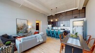 Located at 215 N Webster Ave in Green Bay, Wisconsin, this single-floor unit showcases a thoughtfully designed open-concept layout that seamlessly connects the living, dining, and kitchen areas. Soaring ceilings with exposed structural detailing lend an industrial character throughout, while light hardwood flooring unifies the main living spaces.

The kitchen is a standout feature, outfitted with rich dark cabinetry, a classic white subway tile backsplash, stainless steel appliances, and a spacious island with a light quartz countertop offering bar seating. A geometric decorative panel above the cabinetry adds architectural interest, and pendant lighting with warm-toned globes creates an inviting atmosphere.

The living area benefits from oversized black-framed windows that flood the space with natural light and offer views of the surrounding Green Bay neighborhood. These tall windows contribute to the airy, loft-like feel of the unit.

The bedroom is carpeted for comfort and features similarly tall ceilings and large windows that bring in abundant daylight. An adjoining bathroom is accessible directly from the bedroom. The bathrooms feature dark penny-tile flooring, dark vanity cabinetry with marble-style countertops, white subway tile accents, and distinctive industrial copper pendant lighting, creating a cohesive and stylish aesthetic throughout.