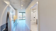 Located in Chicago's vibrant River North neighborhood, this thoughtfully designed studio at 169 W Huron St makes efficient use of its single-floor layout. The space immediately impresses with its exposed concrete ceiling, which lends an industrial-chic character throughout, complemented by light hardwood flooring that runs seamlessly from room to room.

The kitchen is a standout feature, outfitted with two-tone cabinetry — gray shaker-style lower cabinets paired with crisp white uppers — stainless steel appliances including a gas range, built-in microwave, refrigerator, and dishwasher, as well as a herringbone tile backsplash and a matte black faucet over a single-basin sink. Light quartz countertops tie the design together with a clean, modern aesthetic.

The main living area is bathed in natural light courtesy of expansive floor-to-ceiling windows with dark metal framing, offering sweeping views of the surrounding Chicago cityscape and rooftops — a striking urban panorama that amplifies the sense of openness.

The bathroom is equally well-appointed, featuring large-format white tile flooring, a full soaking tub with white subway tile surround, matte black fixtures, and a gray shaker-style vanity with a white countertop and a backlit mirror. The overall ambiance of the space is modern, clean, and urban, with industrial touches that give it a distinctive character.