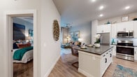 This well-designed single-floor residence offers a seamless blend of modern style and comfortable living. The open-concept layout connects the kitchen and living area, creating an inviting, airy atmosphere ideal for both relaxing and entertaining. The kitchen is a standout, featuring crisp white shaker cabinetry with matte black hardware, dark quartz countertops, a subway tile backsplash, under-cabinet lighting, stainless steel appliances, and a generously sized island with seating — perfect for casual dining or meal prep. Wood-look flooring flows throughout the entire residence, lending warmth and visual continuity. The living area is bright and welcoming, benefiting from large windows and French doors that invite natural light and provide access to a private outdoor balcony. The bedroom is a serene retreat, highlighted by tall ceilings, soft neutral tones, and ample natural light. A second bedroom provides flexible use as a guest room or home office. The bathroom is finished with white cabinetry, dark quartz countertops, a framed mirror, and a tub-shower combination. An in-unit laundry area adds everyday convenience. Decorative wall art and thoughtful design details throughout give the space a curated, contemporary character.