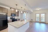 Located at 430 Mosby Blvd in Berryville, Virginia, this well-appointed 2-bedroom, 2-bathroom single-floor residence offers a thoughtfully designed open-concept layout. The combined kitchen, dining, and living area forms the heart of the home, anchored by a large granite-topped kitchen island with a built-in sink and pendant lighting overhead. Rich taupe cabinetry, black appliances, and light wood-style flooring give the kitchen a clean, modern aesthetic. French doors at the end of the living area lead directly to a private patio, filling the space with natural light and providing seamless indoor-outdoor access. A dedicated pantry adds extra storage convenience near the kitchen. Both bedrooms are carpeted and feature windows with neighborhood views, offering a quiet and comfortable retreat. Each bedroom is supported by its own closet, with wire shelving systems for organized storage. The two bathrooms are finished with dark wood vanities, white countertops, and light wood-style flooring. One bathroom is equipped with accessibility grab bars throughout. The overall ambiance of this residence is bright, clean, and functional, with a neutral color palette that lends itself to a variety of décor styles.
