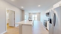 Located on Garland Avenue in Norwalk, Iowa, this well-appointed one-bedroom, one-bathroom residence offers a thoughtfully designed single-level layout with a clean, modern aesthetic throughout. The open-concept kitchen and living area serves as the heart of the home, showcasing white shaker cabinetry, bright white quartz countertops, a spacious island with an undermount sink, and a full suite of stainless steel appliances including a French door refrigerator, electric range, built-in microwave, and dishwasher. Warm-toned luxury vinyl plank flooring runs throughout the main living areas, complementing the neutral wall palette and recessed lighting. The living area extends to a private balcony through sliding glass doors, offering pleasant outdoor views. The bedroom is carpeted for comfort, features a ceiling fan, and is bathed in natural light from a large window. The bathroom includes a white vanity with ample cabinetry and a wide mirror. A dedicated closet with wire shelving provides organized storage. Completing the unit is a convenient in-unit laundry space housing a stacked washer and dryer, with additional wire shelving for storage. The overall ambiance is fresh, clean, and move-in ready.