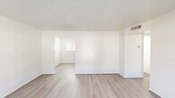 Located at 365 West Pierson Street in Phoenix, AZ, this single-story 3-bedroom, 1-bathroom home offers a clean, modern aesthetic throughout. Light-toned luxury vinyl plank flooring runs continuously across all rooms, complemented by crisp white walls and textured ceilings that create a bright, cohesive feel.

The spacious primary bedroom features white shiplap-style walls, a large mirrored sliding-door closet, and natural light filtering through window blinds. The two additional bedrooms also showcase white-painted brick or shiplap accent walls with windows that bring in outdoor views of surrounding greenery. Each room is well-proportioned and includes closet storage, with four closets total across the home.

The combined kitchen and dining area is efficiently designed with two-tone cabinetry — dark lower cabinets and gray upper cabinets — paired with a white subway tile backsplash, a stainless steel sink, and white appliances including a refrigerator and electric range. Track lighting illuminates the workspace effectively.

The full bathroom is finished with neutral tile flooring, a tub/shower combo, and a vanity with a gray countertop. A glass-panel door in the living/dining area opens to an outdoor area, adding natural light and convenient outdoor access. The hallway connects all rooms with practical flow throughout the home.