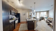 This thoughtfully designed 1-bedroom, 1-bathroom unit offers an efficient and functional single-floor layout. The open-concept kitchen and living area serves as the heart of the home, where rich hardwood flooring and pendant lighting set an inviting tone. The kitchen is outfitted with dark espresso cabinetry, granite countertops, stainless steel appliances, and a central island with bar seating — ideal for both cooking and casual dining. A hallway with an arched entryway connects the main living space to the private areas of the unit.

The living room is comfortably scaled, featuring plush carpeting, large windows with curtain panels, and direct access to a private balcony overlooking a landscaped courtyard. The bedroom offers carpet flooring, a ceiling fan, natural light from a side window, and access to a dedicated closet. The bathroom is finished with a granite-topped vanity, dark wood cabinetry, a framed mirror, and wood-look flooring, maintaining a consistent design aesthetic throughout. A hallway provides a clear and organized transition between all rooms, contributing to the overall sense of flow and practicality within the unit.