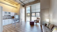 Located on Liberty Avenue in Pittsburgh's 15224 zip code, this one-bedroom, one-bathroom loft-style unit blends industrial character with modern finishes across a single floor. The open-concept living and kitchen area is the heart of the space, distinguished by dramatic soaring ceilings with exposed concrete soffits and visible conduit — hallmarks of its industrial design heritage. Wide-plank hardwood flooring runs throughout, unifying the layout.

Floor-to-ceiling windows flood the living area with abundant natural light, offering street-facing views and creating an airy, expansive feel despite the unit's compact footprint. The kitchen features white cabinetry, granite countertops, a full suite of appliances including a refrigerator, range, and built-in microwave, along with a rolling stainless and granite island for additional prep and dining space.

The bedroom is a cozy, well-defined space, complemented by two closets for ample storage. The bathroom includes a full soaking tub, a single-sink vanity with clean white cabinetry, and wood-tone flooring. A dedicated laundry area adds everyday convenience. Track lighting throughout highlights the loft's architectural details, completing a space that is both functional and full of urban character.