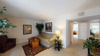 This single-floor residence offers a thoughtfully organized layout that balances comfort and functionality. The living room serves as the heart of the home, featuring plush wall-to-wall carpeting, a textured ceiling, and neutral walls that create a warm, inviting atmosphere. The space accommodates a generous seating arrangement and is accented by framed artwork and lush indoor plants that add character.

The galley-style kitchen is efficiently designed with white cabinetry, dark countertops, hardwood flooring, a full suite of white appliances including a range and refrigerator, and a double basin sink. It opens directly toward the dining area, which features hardwood flooring, a ceiling fan with light fixture, and a window that allows natural light to filter in.

Two bedrooms provide comfortable retreats, each finished with soft carpeting, neutral walls, and windows that bring in natural light. One bedroom includes a sliding closet. The primary bathroom features a walk-in shower with a framed glass door and hardwood-style flooring, while the second bathroom offers a full tub-shower combination, also with hardwood-style flooring. Together, the rooms provide a cohesive, livable environment with practical finishes and a consistent, understated aesthetic throughout.