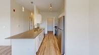 Located in the Copper Creek community in Jackson, Tennessee, this single-floor unit offers a clean, contemporary design throughout. Light-toned, wood-look plank flooring runs consistently across the entire space, complementing the crisp white walls and creating a bright, cohesive aesthetic.

The kitchen is a functional highlight, featuring white shaker-style cabinetry, stone countertops with a built-in sink, and a full suite of stainless steel appliances including a refrigerator, electric range, and microwave. Track lighting and pendant fixtures illuminate the space effectively, while the open layout connects the kitchen to the surrounding living areas.

Multiple living and bedroom spaces are present throughout the unit, each benefiting from natural light provided by white-framed windows fitted with horizontal blinds. Several rooms offer outdoor views of the surrounding landscape, and one room includes direct outdoor access through a glass door, paired with a ceiling fan overhead. Accessibility features are noted in the bathroom, which includes grab bars and hard-surface flooring.

A dedicated laundry room houses a full-size washer and dryer with overhead wire shelving for additional storage. Throughout the unit, clean lines, neutral tones, and consistent finishes contribute to a modern, move-in-ready living environment.